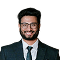 Professional headshot of a bearded man with glasses, wearing a dark suit and blue tie, smiling at the camera.