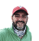 Smiling man wearing a green shirt and red baseball cap, posing for a photo outdoors.
