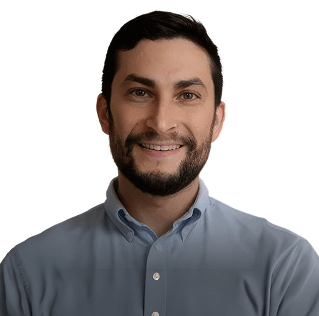 Portrait of a smiling man with dark hair and a beard, wearing a light blue button-down shirt.