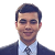 Professional headshot of a man in a dark suit and blue tie, smiling against a light gray background.