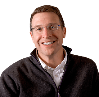 Smiling man with short brown hair and glasses, wearing a white collared shirt and a dark zip-up sweater.